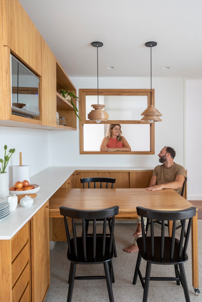 Apê de 300 m² tem sala íntima com TV e cozinha com armários amarelos. Projeto de PKB Arquitetura. Na foto, copa de cozinha com mesa de madeira e cadeiras de madeira preta, bancada branca.
