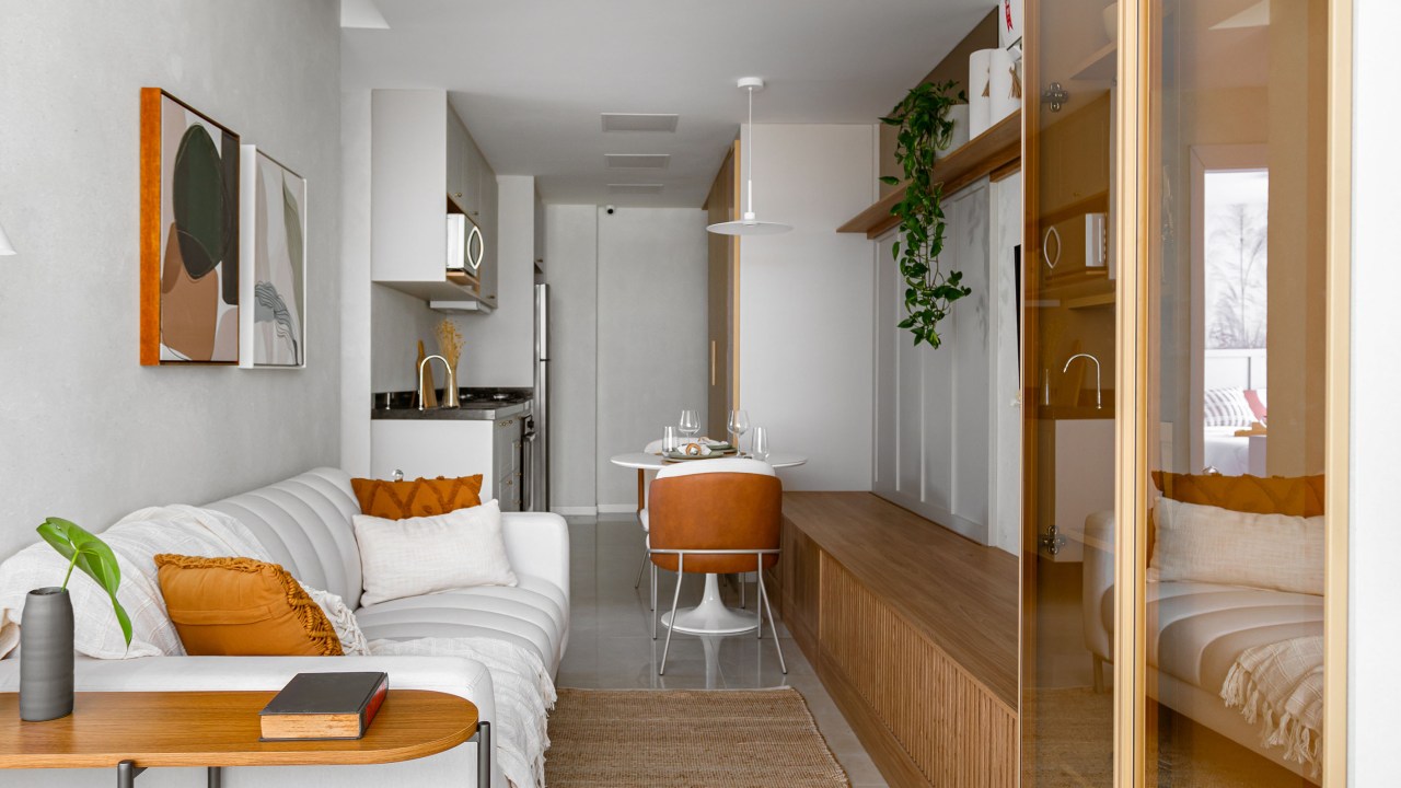 Apê de 56 m² com varanda foi projetado para família de 4 pessoas. Projeto de NOP Arquitetura. Na foto, sala de estar com sofá branco, tapete, mesinha lateral em madeira.