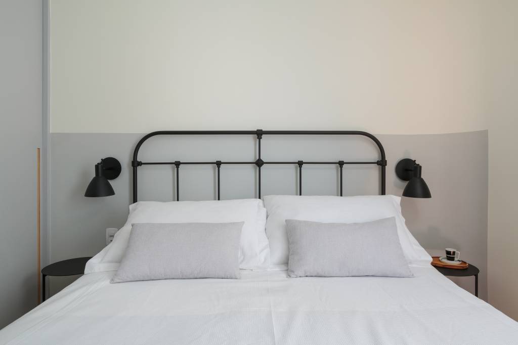 Apê de 70 m² ganha toque industrial com viga aparente e cama em metal. Projeto de Estúdio Maré. Na foto, quarto com meia parede cinza clara, cama de metal.