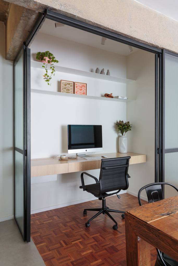 Apê de 70 m² ganha toque industrial com viga aparente e cama em metal. Projeto de Estúdio Maré. Na foto, home office delimitado por portas de correr de vidro canelado.