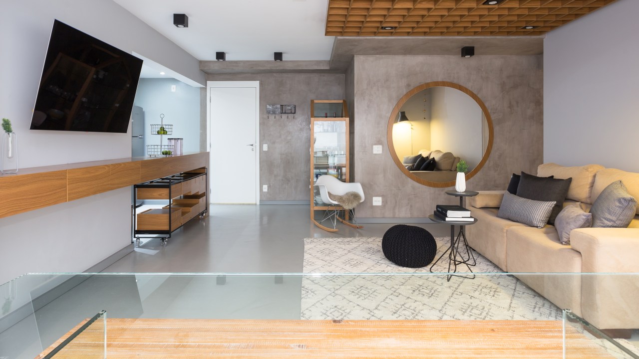 Apê de 89 m² ganha paredes com cimento queimado e piso com camada de epóxi. Projeto de Ju Matos. Na foto, sala de estar, espelho redondo.
