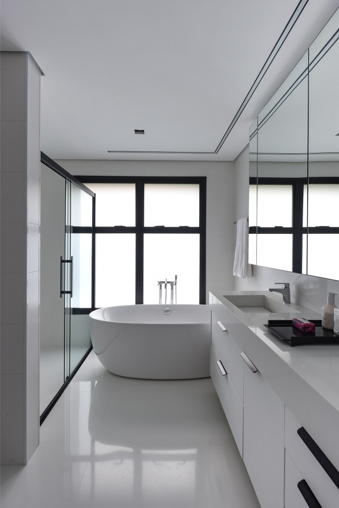 Apê industrial de 360 m² é inspirado nos lofts de Nova York. Projeto de Rebeca Catalucci. Na foto, banheiro com móveis brancos. Banheira de apoio.
