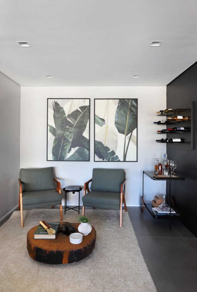 Apê em tons de preto de 91 m² tem cantinho de degustação de vinho. Projeto de Fantato Nitoli Arquitetura. Na foto, cantinho de bar com duas poltronas verdes, adega, tapete e quadros na parede.