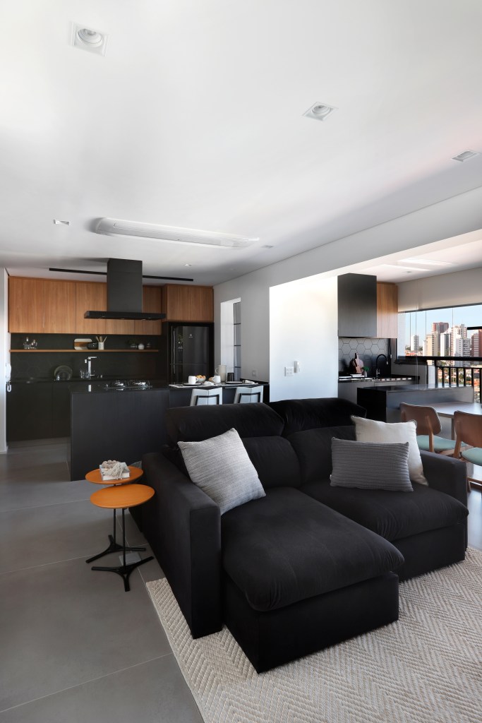 Apê em tons de preto de 91 m² tem cantinho de degustação de vinho. Projeto de Fantato Nitoli Arquitetura. Na foto, sala integrada com cozinha, sofá preto.