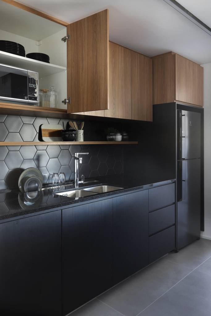 Apê em tons de preto de 91 m² tem cantinho de degustação de vinho. Projeto de Fantato Nitoli Arquitetura. Na foto, cozinha integrada backsplash preto, ilha e piso de porcelanato.