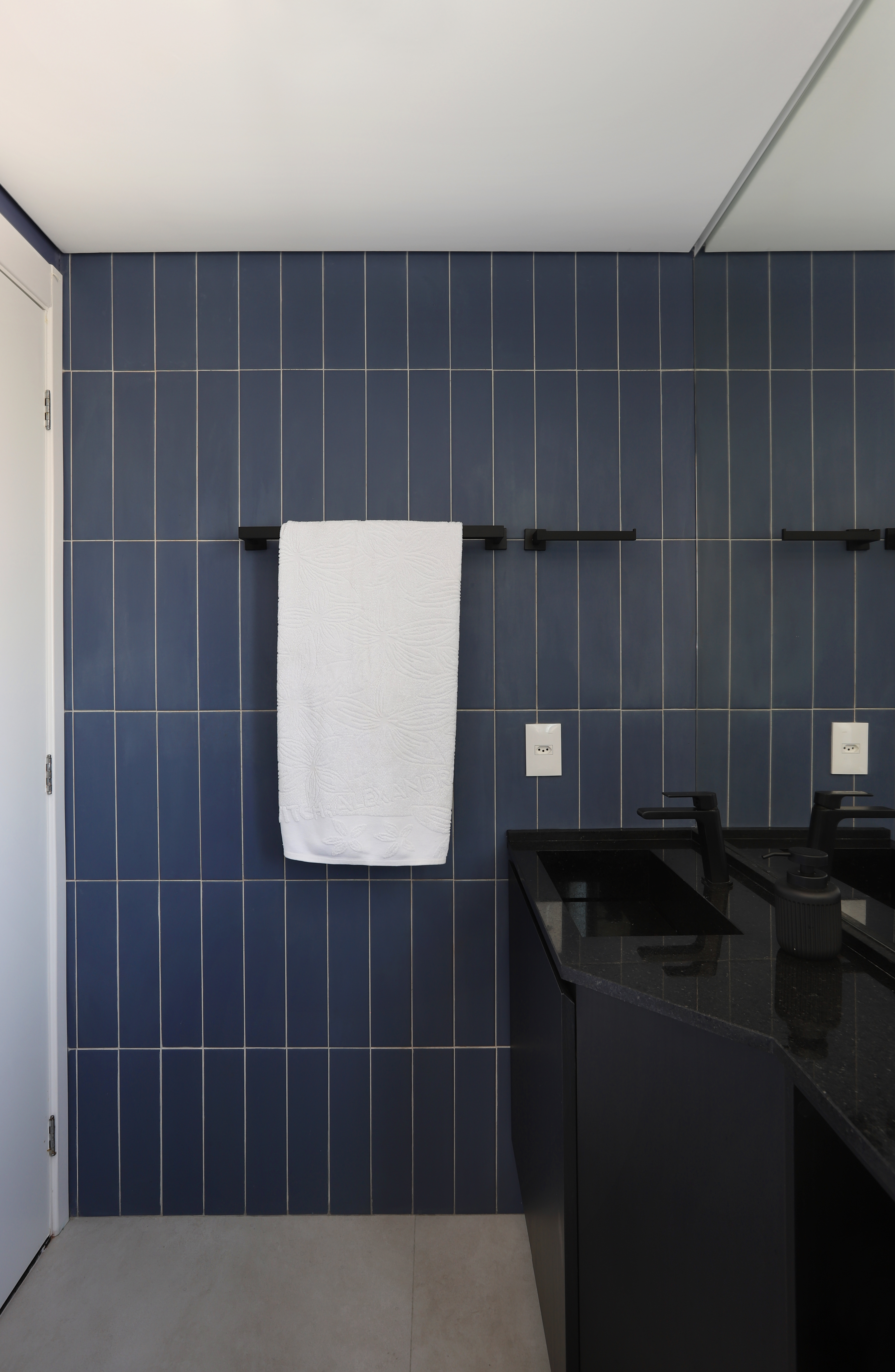 Apê em tons de preto de 91 m² tem cantinho de degustação de vinho. Projeto de Fantato Nitoli Arquitetura. Na foto, banheiro com parede de ladrilhos azuis, bancada e metais pretos.