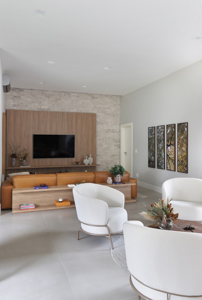 Área gourmet aconchegante é a protagonista desta casa de campo de 600 m². Projeto de Almada Arquitetura. Na foto, sala de estar e tv com painel de madeira, quadros e mesa.