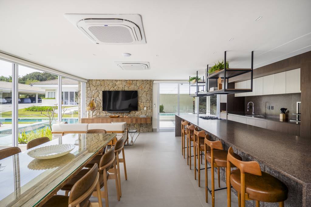 Área gourmet integrada ao jardim é o coração desta casa. Projeto de TM Arquitetura. Na foto, sala de estar na varanda e parede de pedra. Cozinha com ilha.