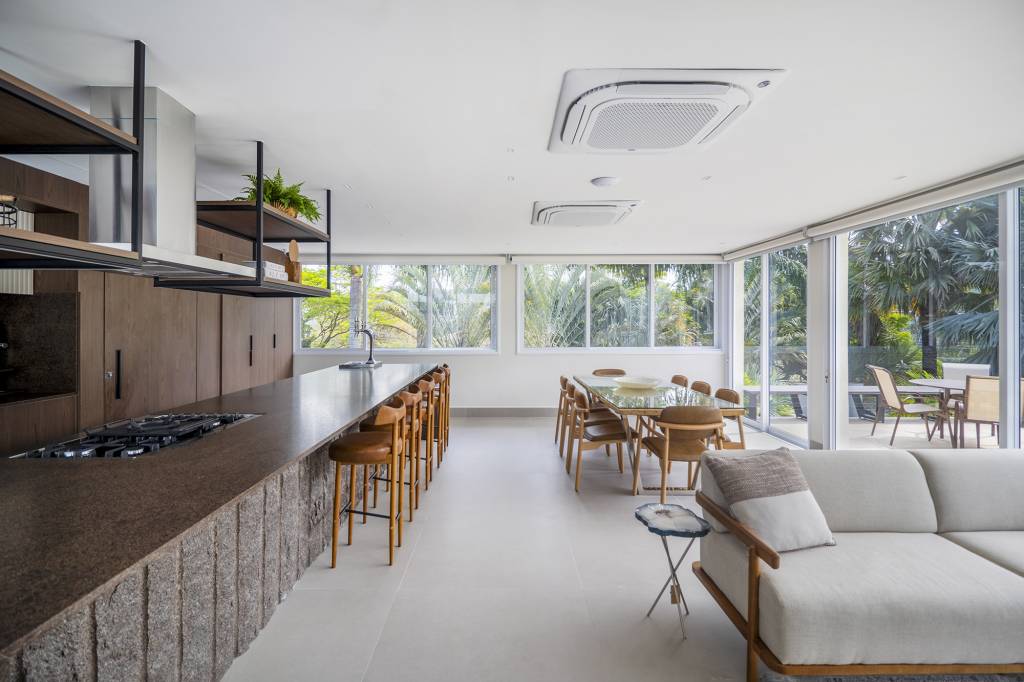 Área gourmet integrada ao jardim é o coração desta casa. Projeto de TM Arquitetura. Na foto, varanda gourmet com ilha, jantar e estar.