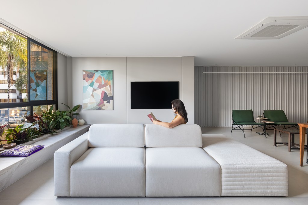 Arte, design e natureza se unem neste apartamento em Brasília. Projeto de Três E+ Arquitetura e Design. Na foto, sala de estar com sofá ilha e tv.