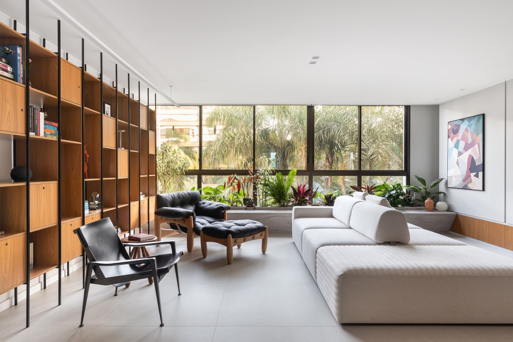 Arte, design e natureza se unem neste apartamento em Brasília. Projeto de Três E+ Arquitetura e Design. Na foto, sala de jantar com quadros, pendentes e estante. Sofá ilha.