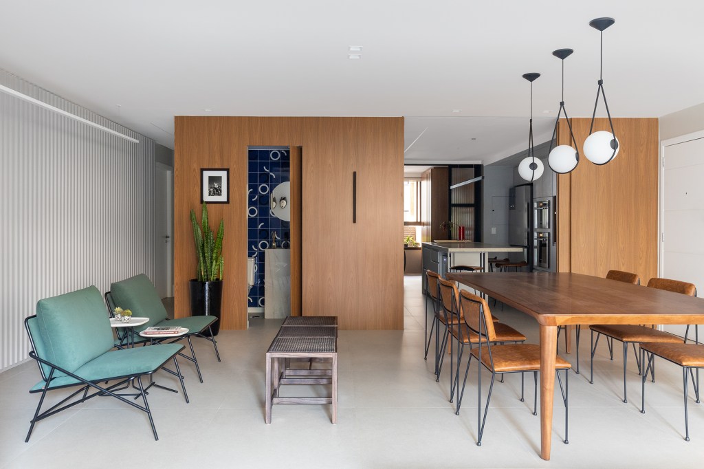 Arte, design e natureza se unem neste apartamento em Brasília. Projeto de Três E+ Arquitetura e Design. Na foto, sala com poltronas, mesa de jantar e painel de madeira.