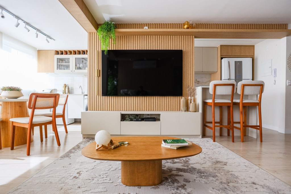Bege, móveis planejados e muita madeira compõem o décor de apê de 95 m². Projeto de Thais Aguiar. Na foto, sala com varanda e lavanderia. Painel ripado de TV.