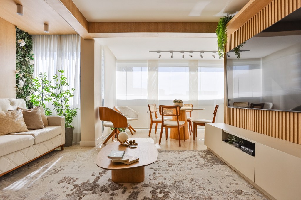 Bege, móveis planejados e muita madeira compõem o décor de apê de 95 m². Projeto de Thais Aguiar. Na foto, sala com varanda integrada e painel ripado de TV.