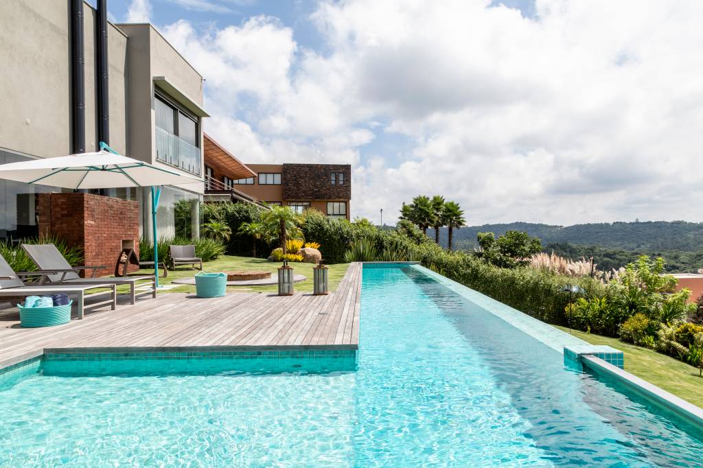 Atemporal e elegante: casa tem lareira e cozinha com piso de ladrilho. Projeto de Carolina Gava. Na foto, fachada de casa, área externa com piscina e deck de madeira.