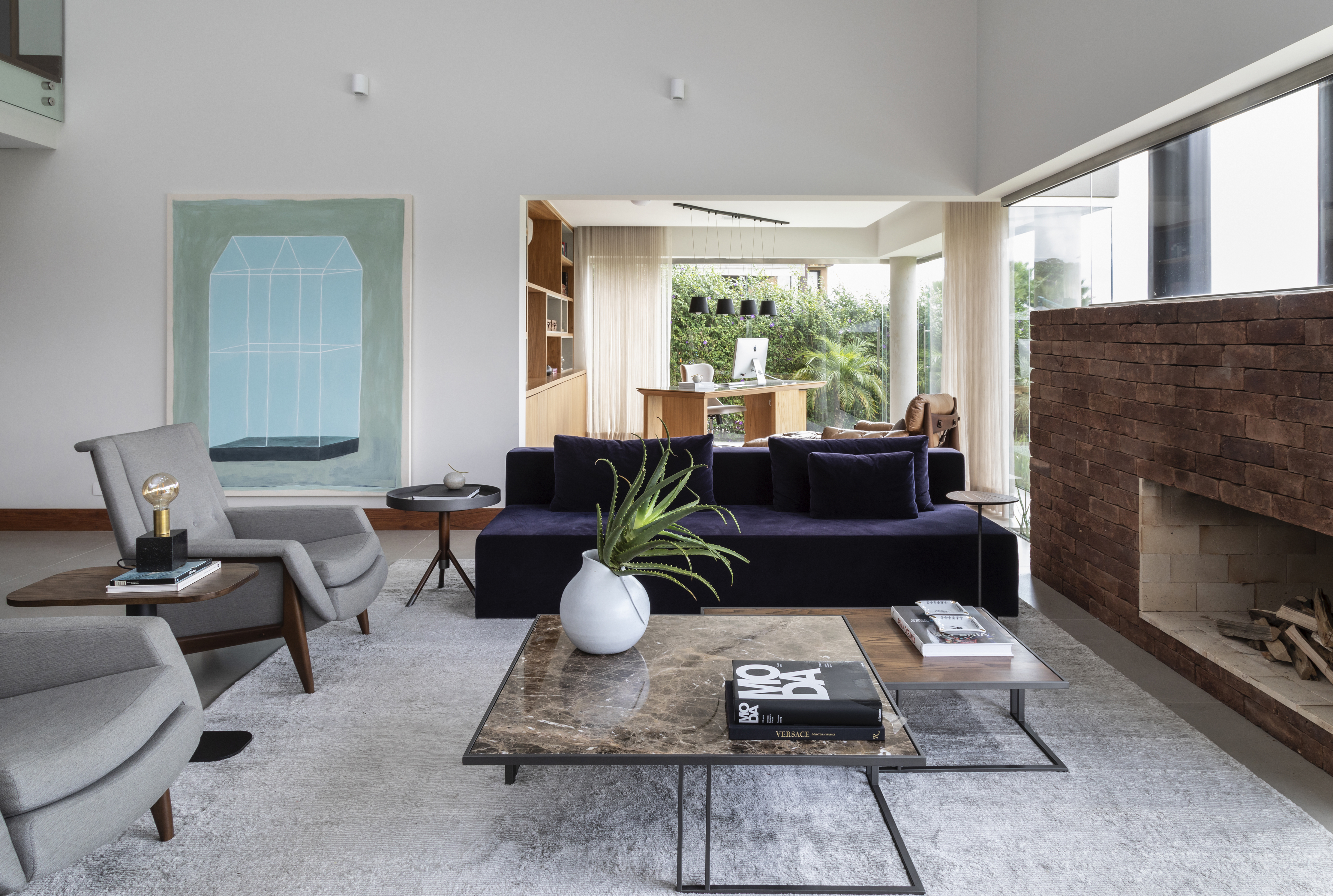 Atemporal e elegante: casa tem lareira e cozinha com piso de ladrilho. Projeto de Carolina Gava. Na foto, sala com mesa de centro grande, sofá azul.