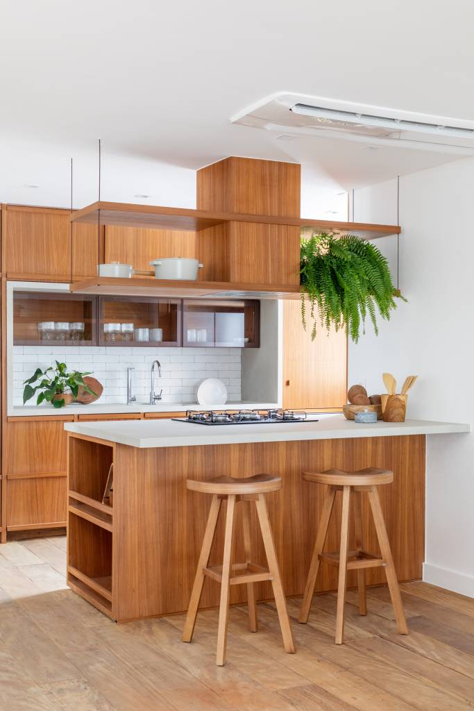 Cobertura de 200 m² ganha piscina com azulejos coloridos e área gourmet. Projeto de Escala Arquitetura. Na foto, cozinha integrada com ilha de tampo branco e banquetas pequenas de madeira.