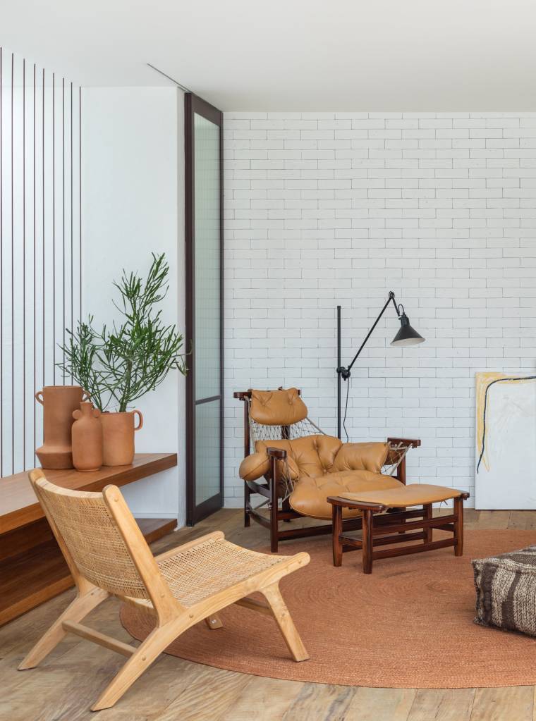 Cobertura de 200 m² ganha piscina com azulejos coloridos e área gourmet. Projeto de Escala Arquitetura. Na foto, sala de estar com tapete em tom terracota, poltrona de madeira, poltrona jangada, luminária de piso, aparador com peças de cerâmica.