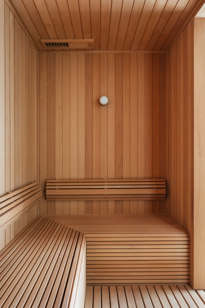 Cobertura tem sauna com paredes de vidro e área gourmet com balanços. Projeto de Vivian Reimers. Na foto, sauna revestida de madeira com banco, porta e parede de vidro.