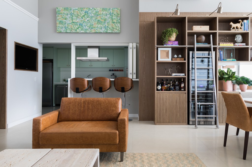 Cores diferentes criam efeitos de altura em apê com pé-direito duplo. Projeto de Caio Nazar. Na foto, sala com estante, jantar e cozinha integrada.