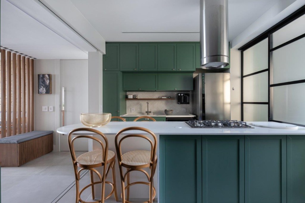 Cores verde, azul, rosa e detalhes em pedra e palha pontuam apê de 180 m². Projeto de Natália Salla. Na foto, cozinha com ilha, coifa, armários verdes, mesa branca, cadeiras de palhinha.