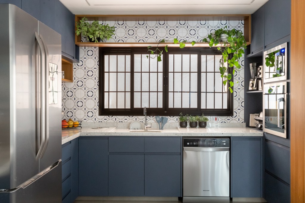 Cozinha com marcenaria azul e toque retrô tem canto alemão e canto do café. Projeto de Camilla Bischoff. Na foto, parede de azulejos, plantas em prateleira, armário azul.