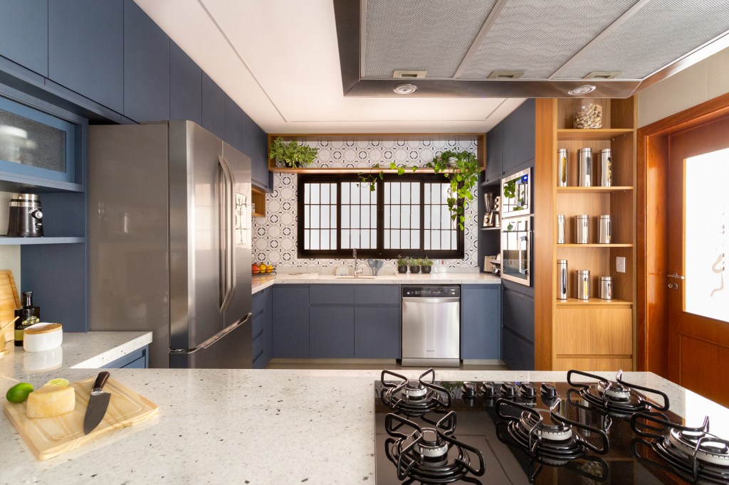 Cozinha com marcenaria azul e toque retrô tem canto alemão e canto do café. Projeto de Camilla Bischoff. Na foto, parede de azulejos, plantas em prateleira, armário azul, bancada branca.