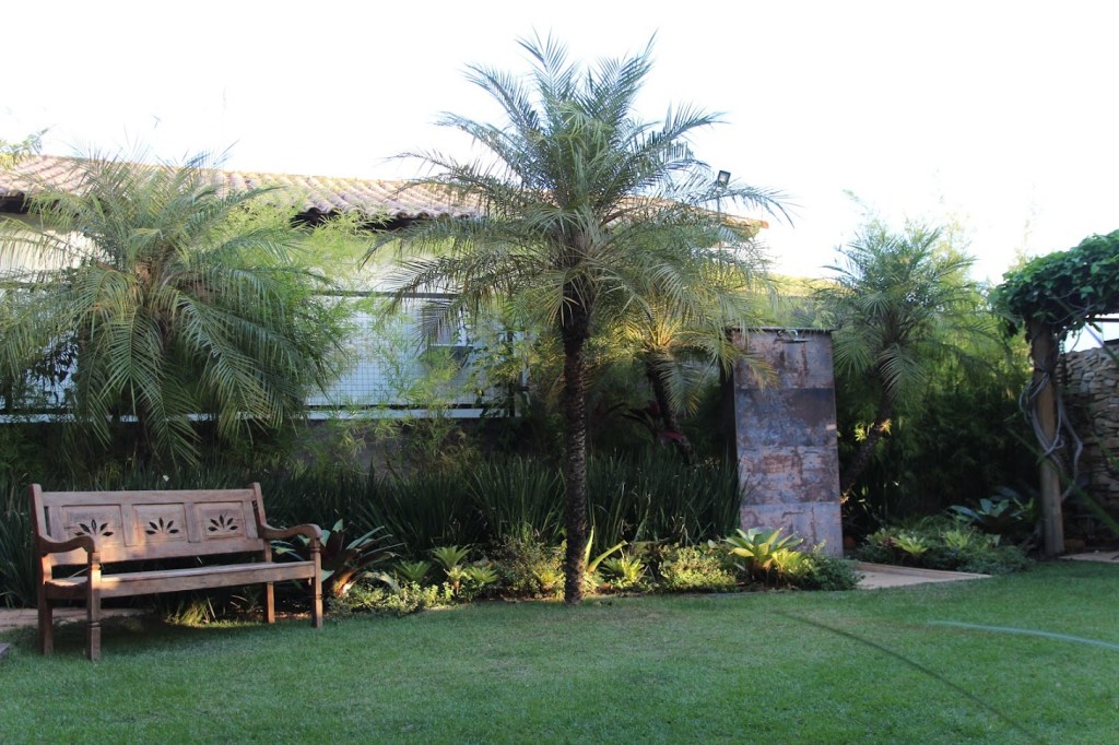 Jardim de 200 m² tem paisagismo tropical e lago que funciona como piscina. Projeto de Júlio Sousa, Na foto, jardim com banco e chuveirão.