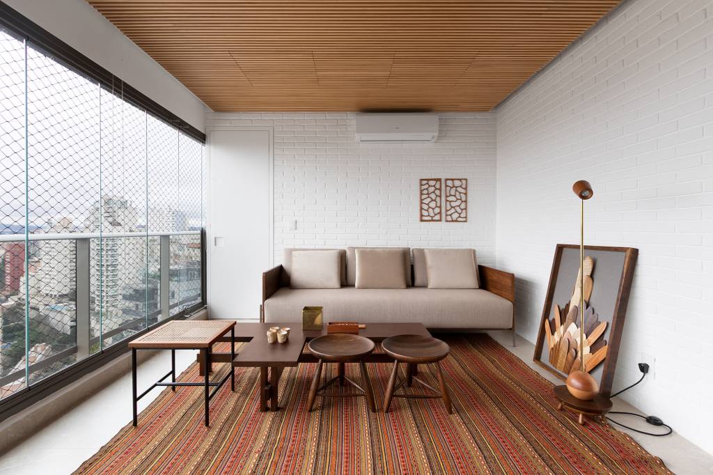 linguagem-neutra-atemporal-decor-apartamento-140-m2-mnbr-arquitetos-credito-alexandre=disanaro (1) Linguagem neutra e atemporal definem o décor de apartamento de 140 m². Projeto MNBR Arquitetos. Na foto, varanda com parede de tijolo, tapete e quadro.