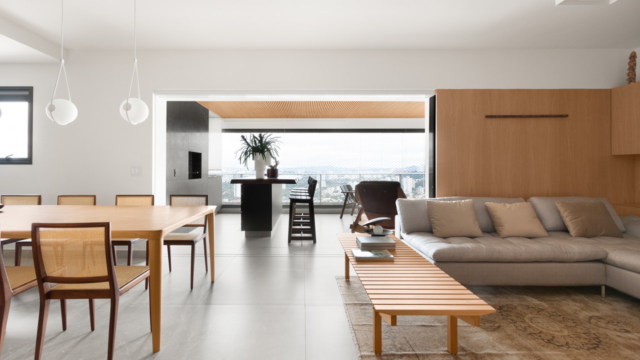 Linguagem neutra e atemporal definem o décor de apartamento de 140 m². Projeto MNBR Arquitetos. Na foto, sala integrada com a varanda e jantar. Paredes de madeira e tapete.