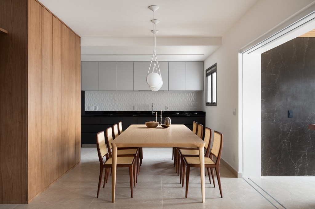 Linguagem neutra e atemporal definem o décor de apartamento de 140 m². Projeto MNBR Arquitetos. Na foto, sala de jantar com mesa de madeira e cozinha integrada,