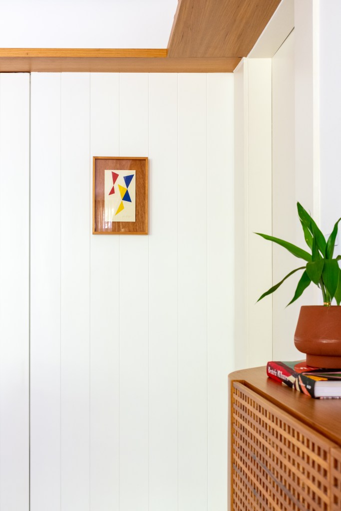 Madeira em tom natural e pintada de branco dão leveza à apê de 117 m². Projeto de Mariana Monnerat e Tainá Binato. Na foto, parede de madeira branca com quadro pequeno.