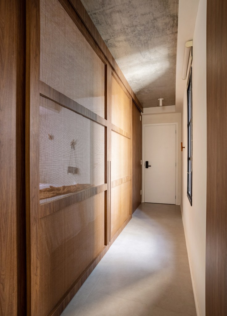 Marcenaria personalizada otimiza espaço e esconde eletros em apê de 48 m². Projeto de Carolina Gava. Na foto, corredor, portas de correr fechadas isolando quartos.