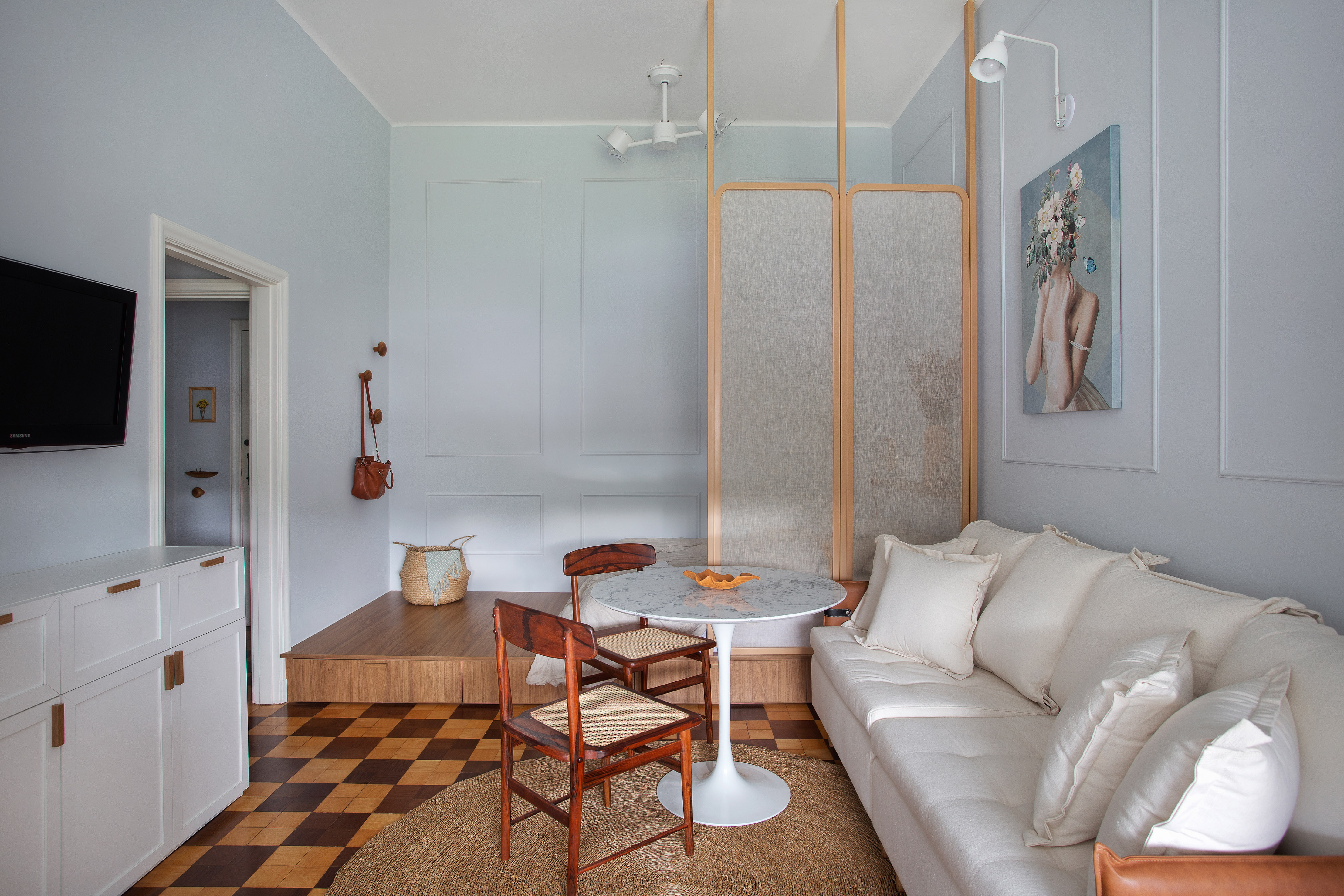 Descubra microapê rococó de apenas 30 m² no hotel-cassino Quitandinha. Projeto de Manuela Fleck. Na foto, sala de estar pequena, sofá branco, divisória transparente, mesa redonda pequena, cadeiras de madeira, piso de madeira.