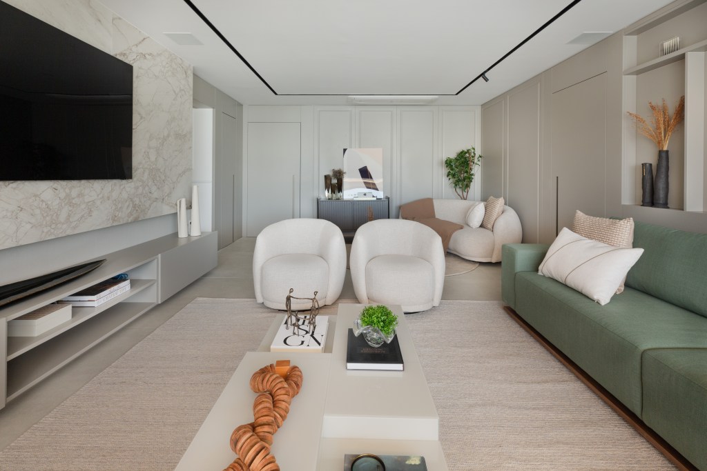 Sofá verde inspira a paleta de cores deste apartamento com décor clássico. Projeto de ADVP. Na foto, sala com sofá curvo e aparador. Sofá verde e tv,