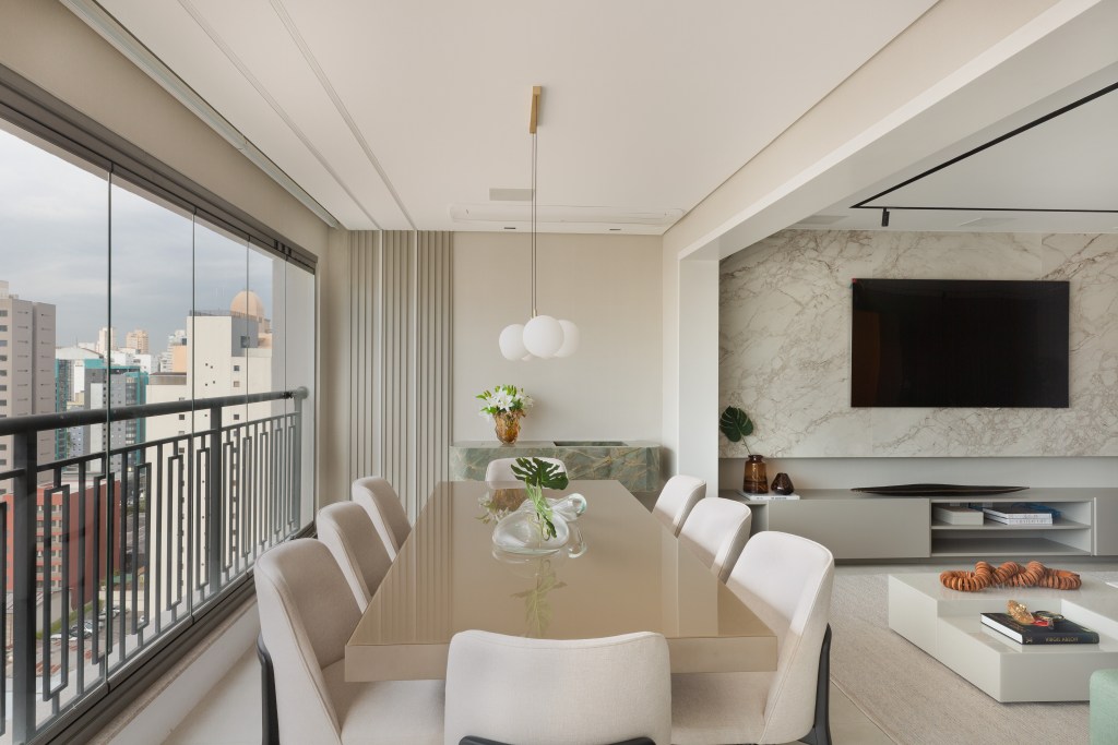 Sofá verde inspira a paleta de cores deste apartamento com décor clássico. Projeto de ADVP. Na foto, varanda com mesa de jantar e tv.