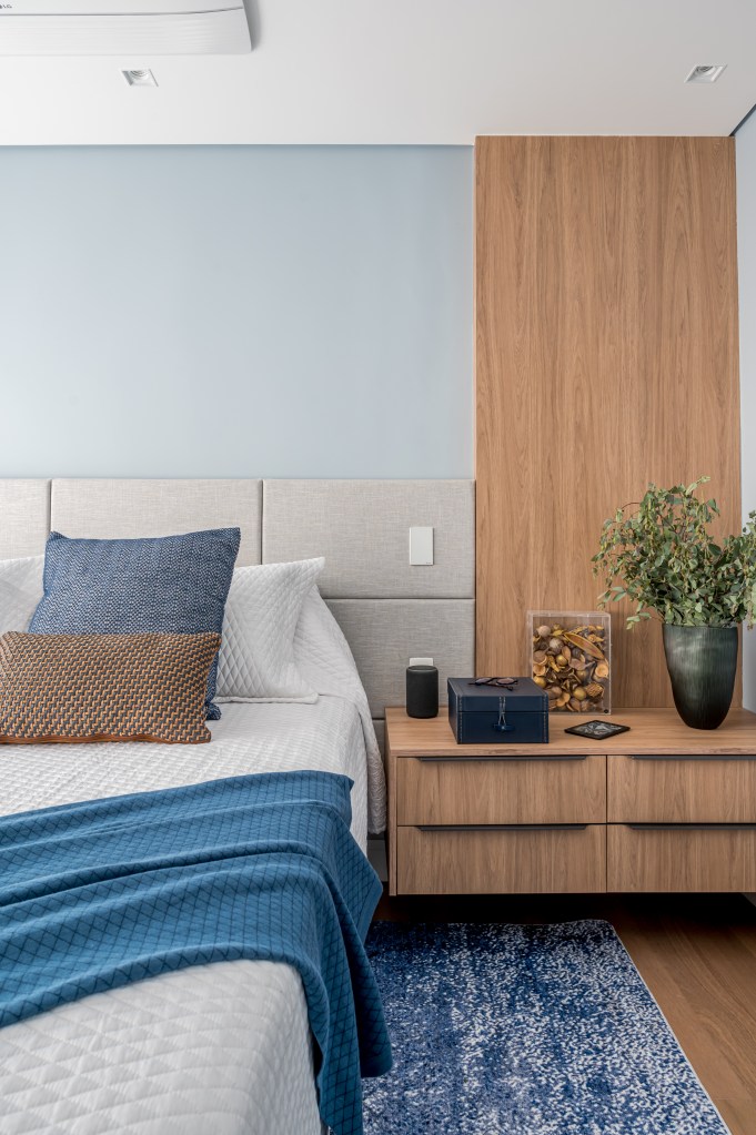 Tons de azul e integração total na área social marcam apê de 107 m². Projeto de Daniela Funari. Na foto, quarto, cabeceira estofada, parede azul, cama de casal, mesa lateral em madeira.