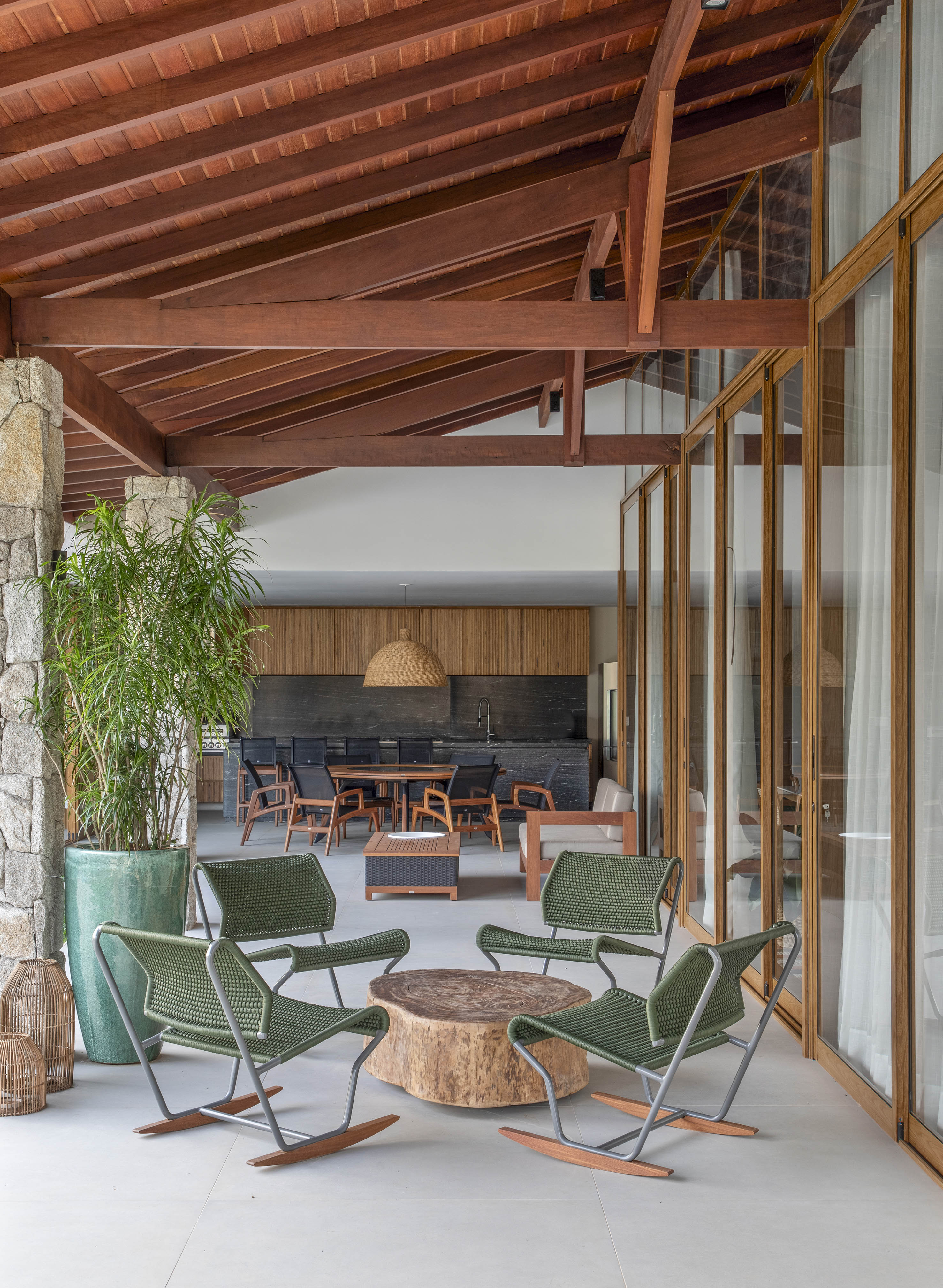 Tons naturais e base neutra marcam casa de campo com cozinha provençal. Projeto de João Panaggio. Na foto, varanda com área gourmet, cadeiras verdes, mesa de centro de madeira.