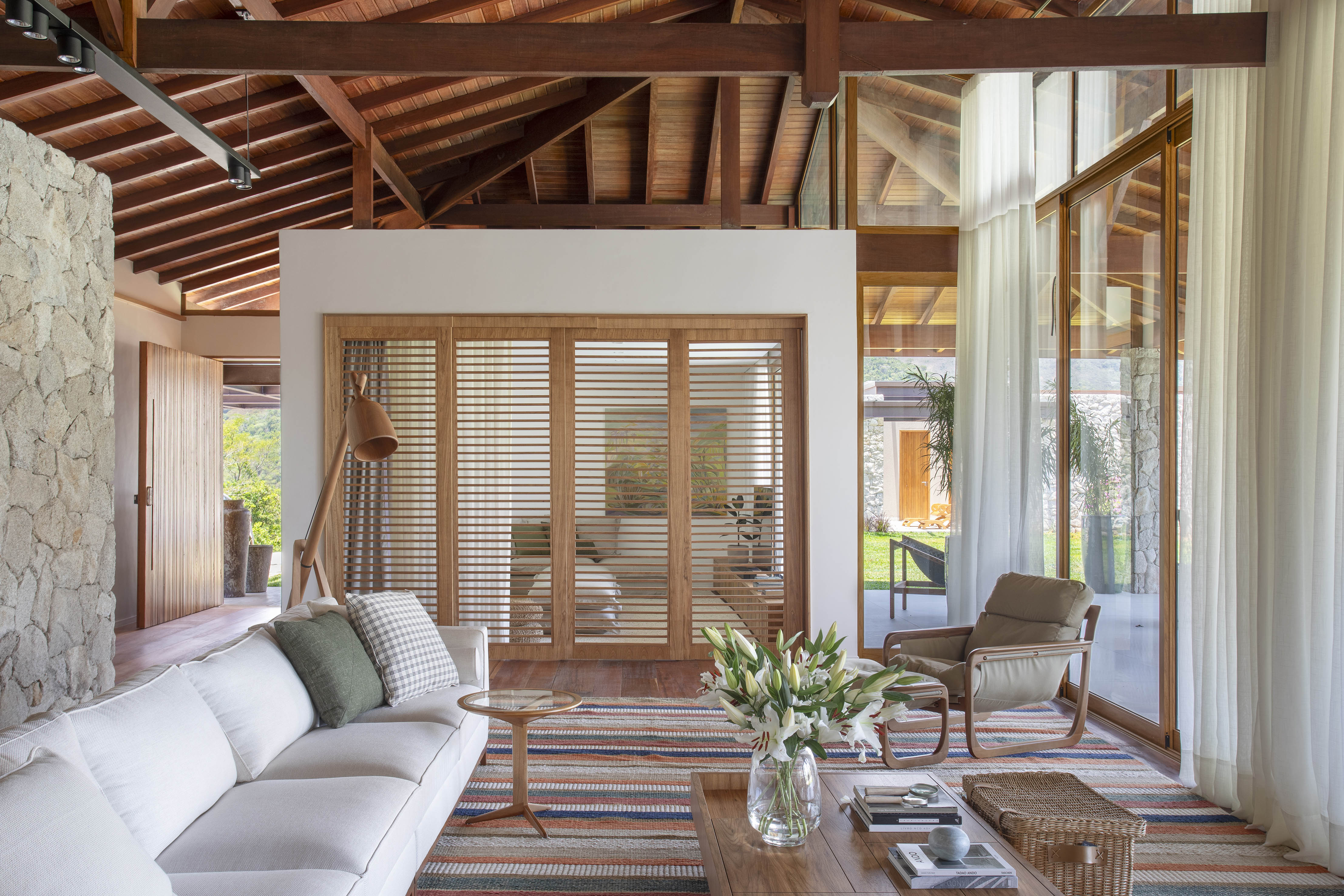 Tons naturais e base neutra marcam casa de campo com cozinha provençal. Projeto de João Panaggio. Na foto, sala de estar com pé-direito duplo, tapete listrado, sofás brancos, mesa de centro.