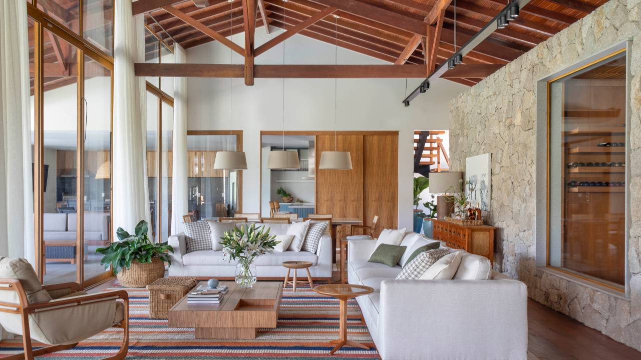 Tons naturais e base neutra marcam casa de campo com cozinha provençal. Projeto de João Panaggio. Na foto, sala de estar com pé-direito duplo, tapete listrado, sofás brancos, mesa de centro.