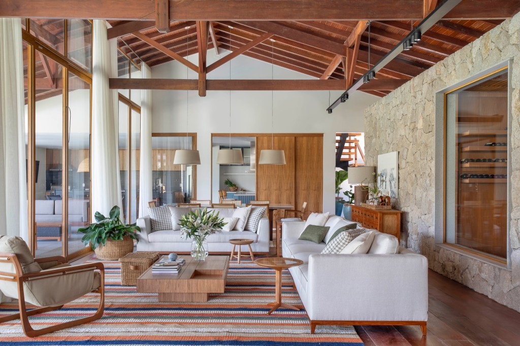 Tons naturais e base neutra marcam casa de campo com cozinha provençal. Projeto de João Panaggio. Na foto, sala de estar com pé-direito duplo, tapete listrado, sofás brancos, mesa de centro.
