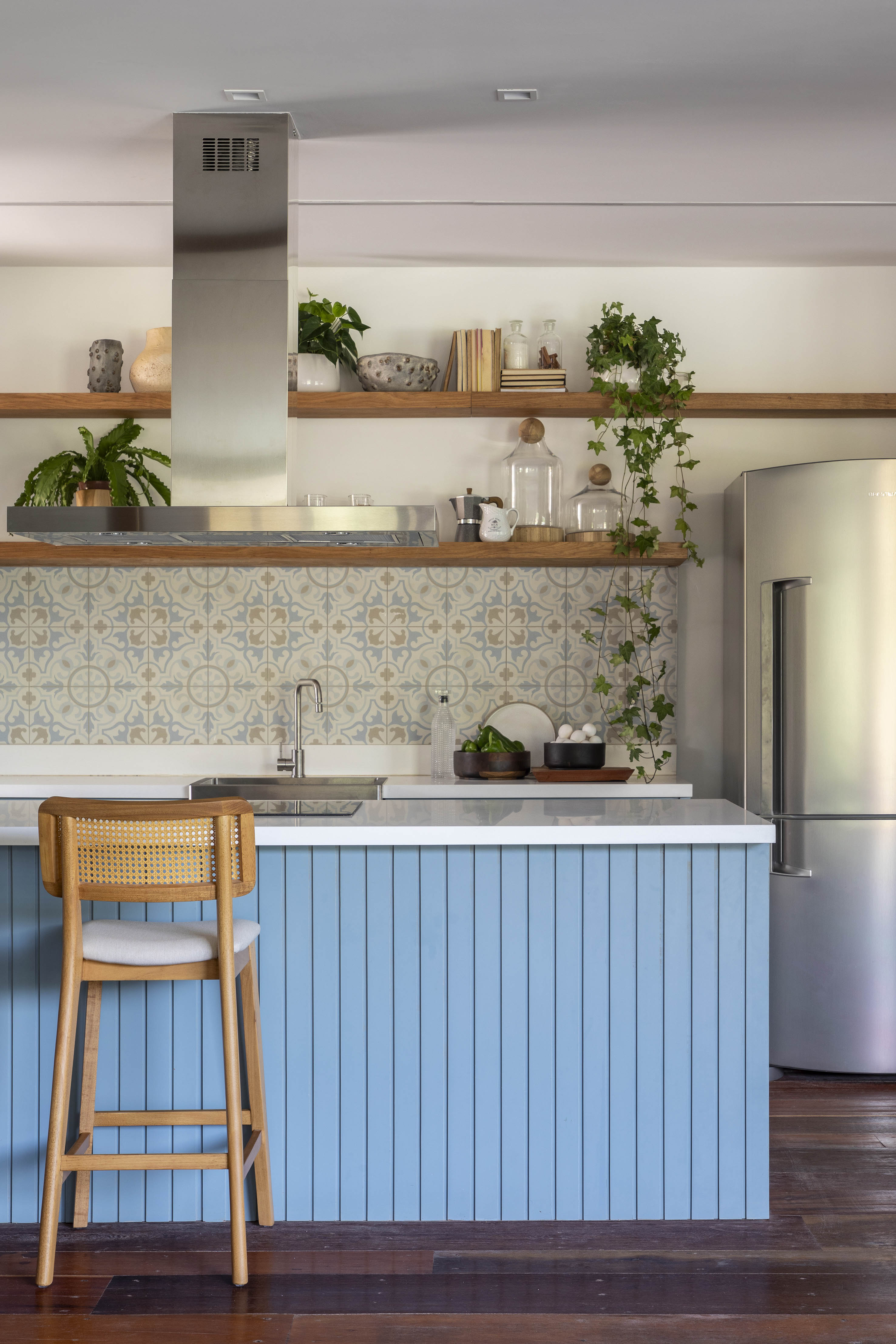 Tons naturais e base neutra marcam casa de campo com cozinha provençal. Projeto de João Panaggio. Na foto, cozinha em estilo provençal, azulejos, ilha com bancada branca e revestimento azul ripado.