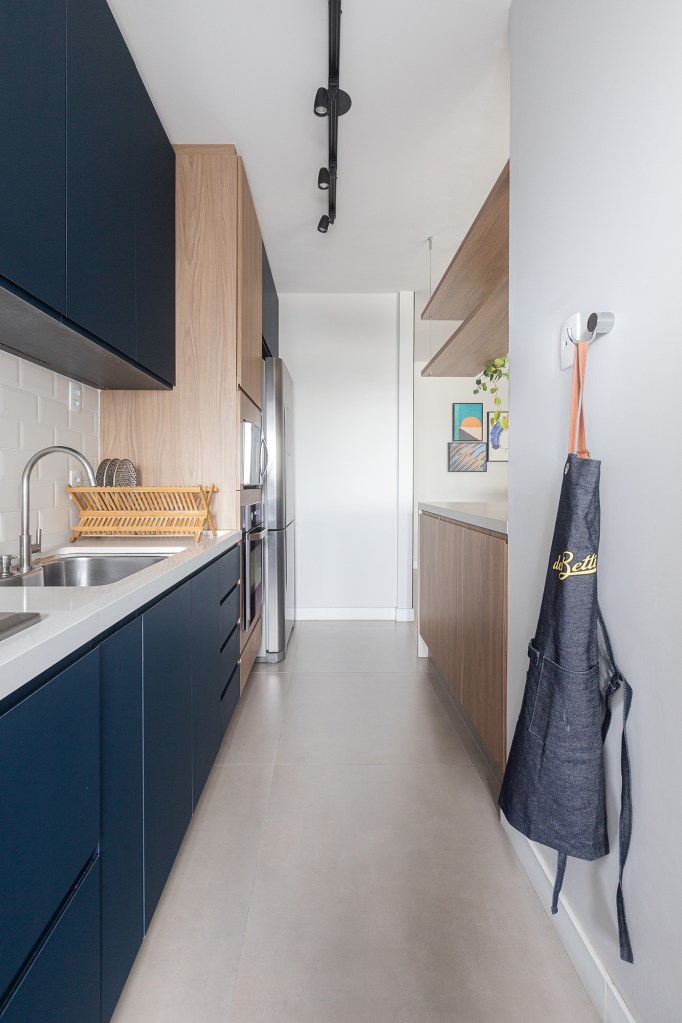 Uma única bancada une área gourmet e cozinha neste apê de 90 m². Projeto de Livia Dalmaso. Na foto, cozinha corredor com marcenaria azul.