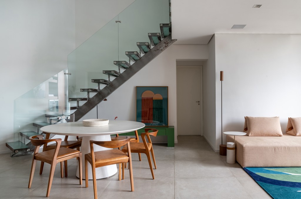 Apartamento de 170 m² com pé-direito duplo tem estúdio de DJ no mezanino. Projeto de Carolina Esper. Na foto, sala de jantar com mesa redonda e escada.