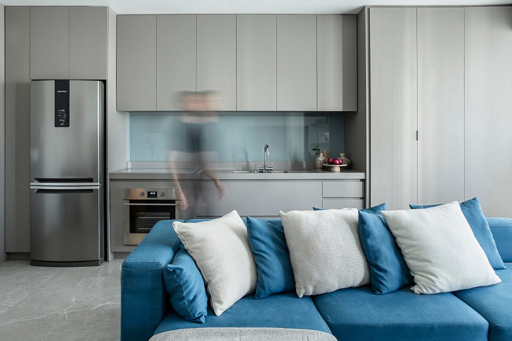 Apartamento de 60 m² ganha décor com tons de azul que remete à praia. Projeto de ETC. Arquitetos. Na foto, sala com sofá azul, cozinha integrada e jantar.