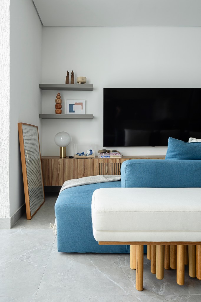 Apartamento de 60 m² ganha décor com tons de azul que remete à praia. Projeto de ETC. Arquitetos. Na foto, sala com sofá azul, cozinha integrada e jantar.