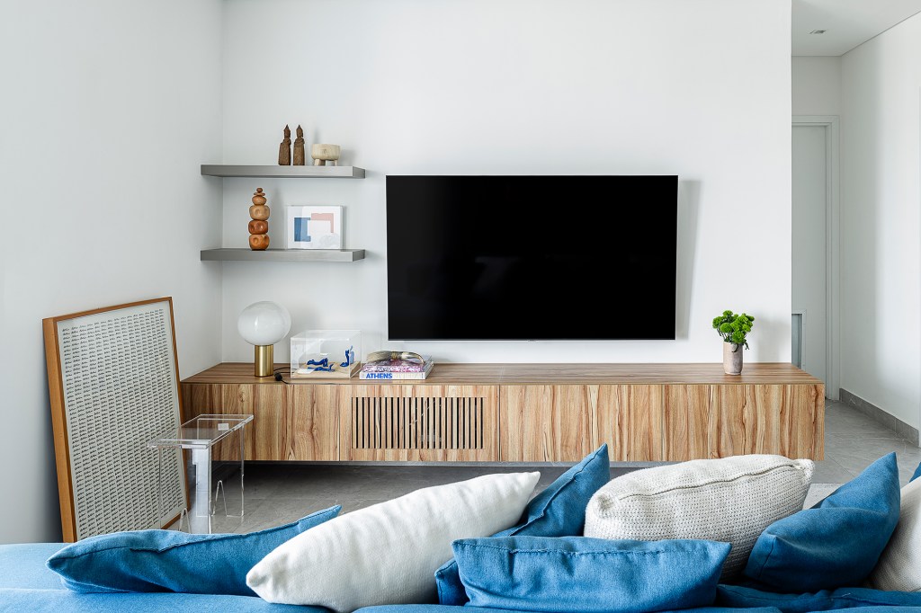 Apartamento de 60 m² ganha décor com tons de azul que remete à praia. Projeto de ETC. Arquitetos. Na foto, sala com varanda, tv e sofá azul.