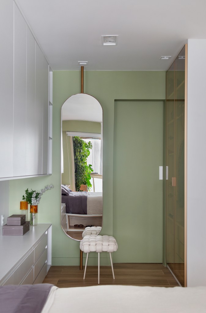 Apê clean de 93 m² tem cuba farm sink, espelho giratório, brises e lambris. Projeto de Manoela Fleck. Na foto, quarto, parede verde, espelho giratório.