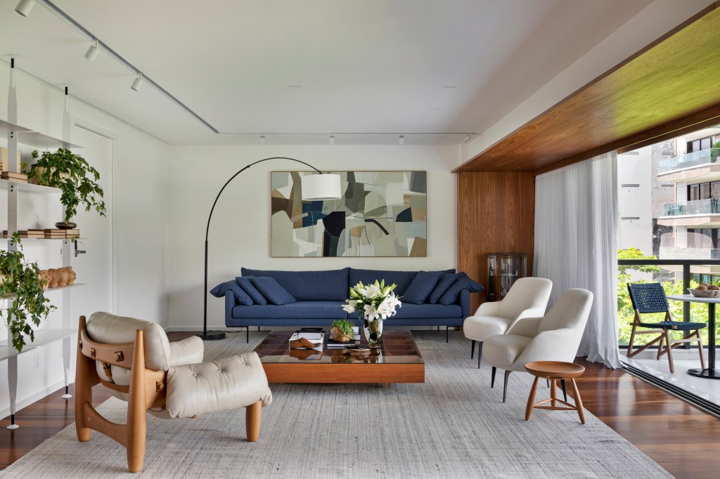 Apê integrado ganha décor contemporâneo com muita marcenaria em freijó. Projeto de João Panaggio. Na foto, sala de estar, sofá azul, quadro, luminária de piso, mesa de centro.