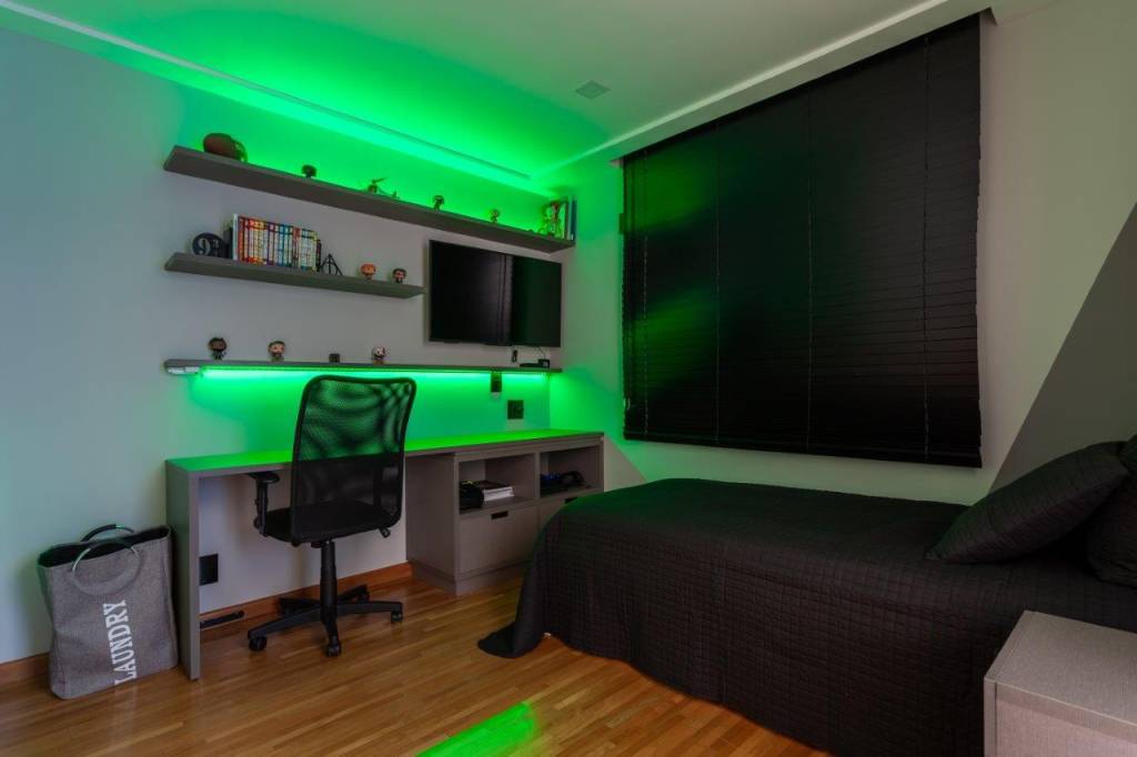 Base neutra com pontos marcantes em azul definem apê de 167 m². Projeto de Ju Miranda. Na foto, quarto de adolescente gamer, persiana, iluminação com luzes LED coloridas.